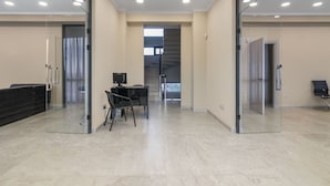 Un espacio de oficina moderno con paredes de vidrio, una recepción, una escalera y un área de reuniones con sillas y una mesa.