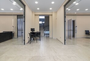 Un espacio de oficina moderno con paredes de vidrio, una recepción, una escalera y un área de reuniones con sillas y una mesa.