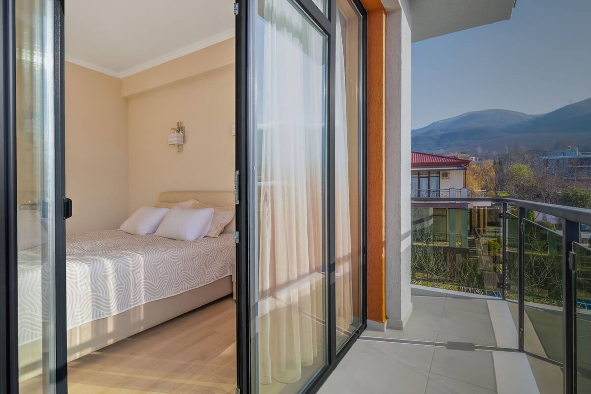 Un dormitorio con cama, mesita de noche y ventana con cortinas.