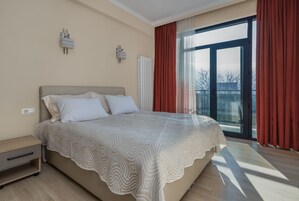 Un dormitorio con una cama grande, una mesita de noche, una lámpara de pared y una ventana con cortinas.