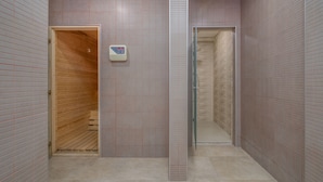 Un baño moderno con sauna de madera, cabina de ducha de vidrio y una balanza digital en la pared.