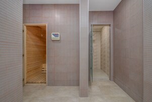 Un baño moderno con sauna de madera, cabina de ducha de vidrio y una balanza digital en la pared.