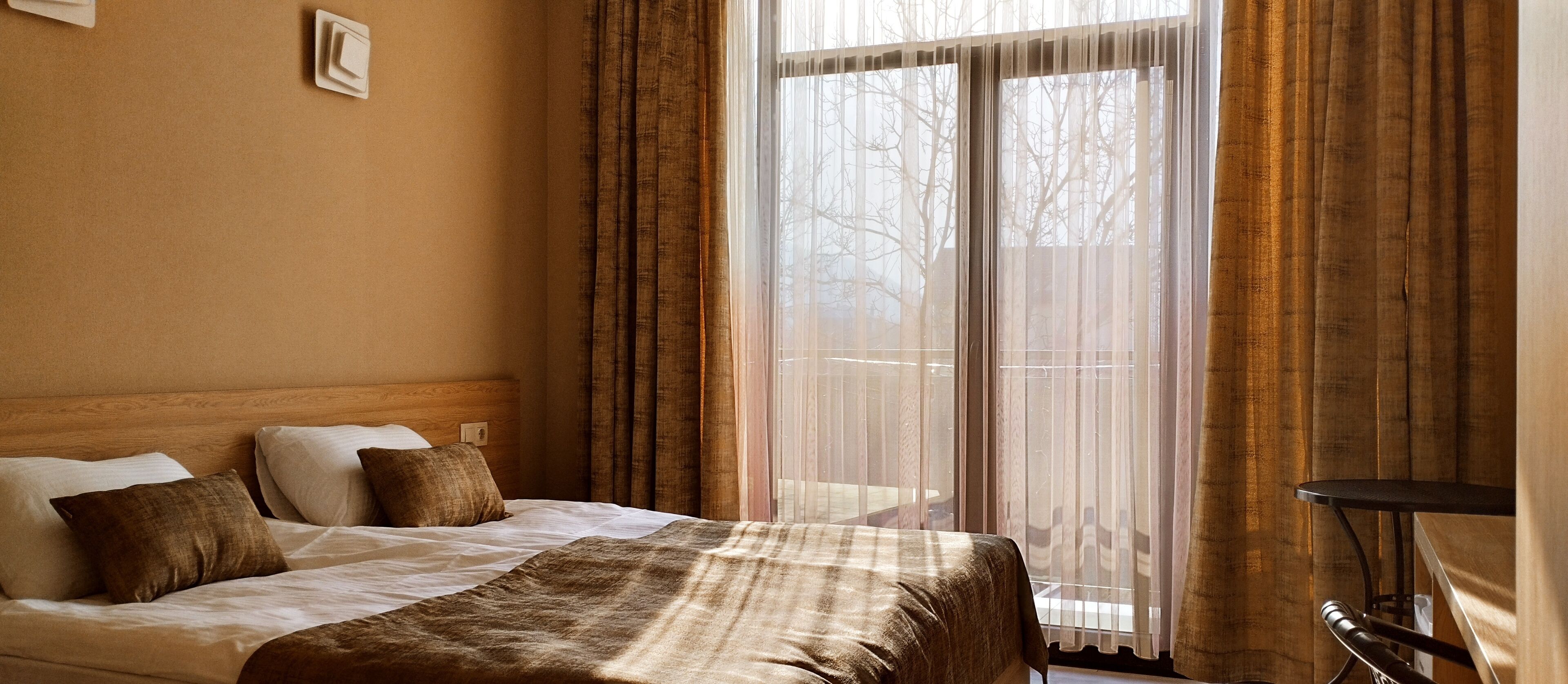 A hotel room with a bed, a bedside table, and a window with curtains.
