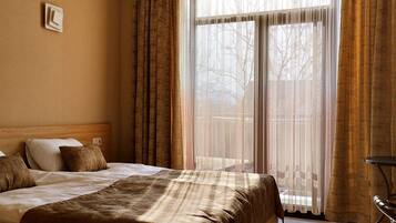 A hotel room with a bed, a bedside table, and a window with curtains.