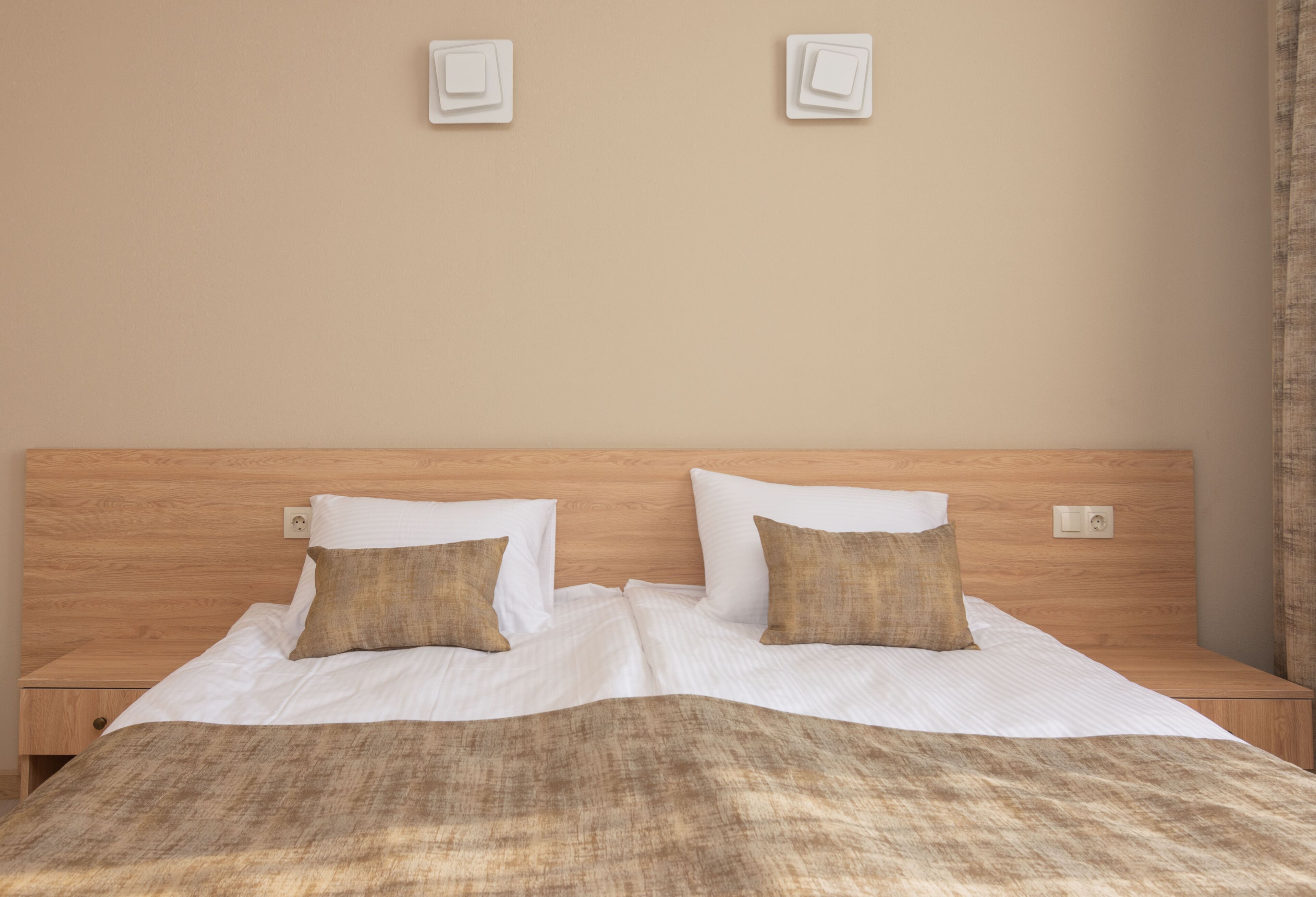 A neatly made bed with two pillows, a wooden headboard, and two bedside tables.