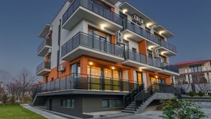 A multi-story residential building with balconies, large windows, and a staircase leading to the entrance.
