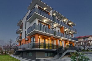 A multi-story residential building with balconies, large windows, and a staircase leading to the entrance.
