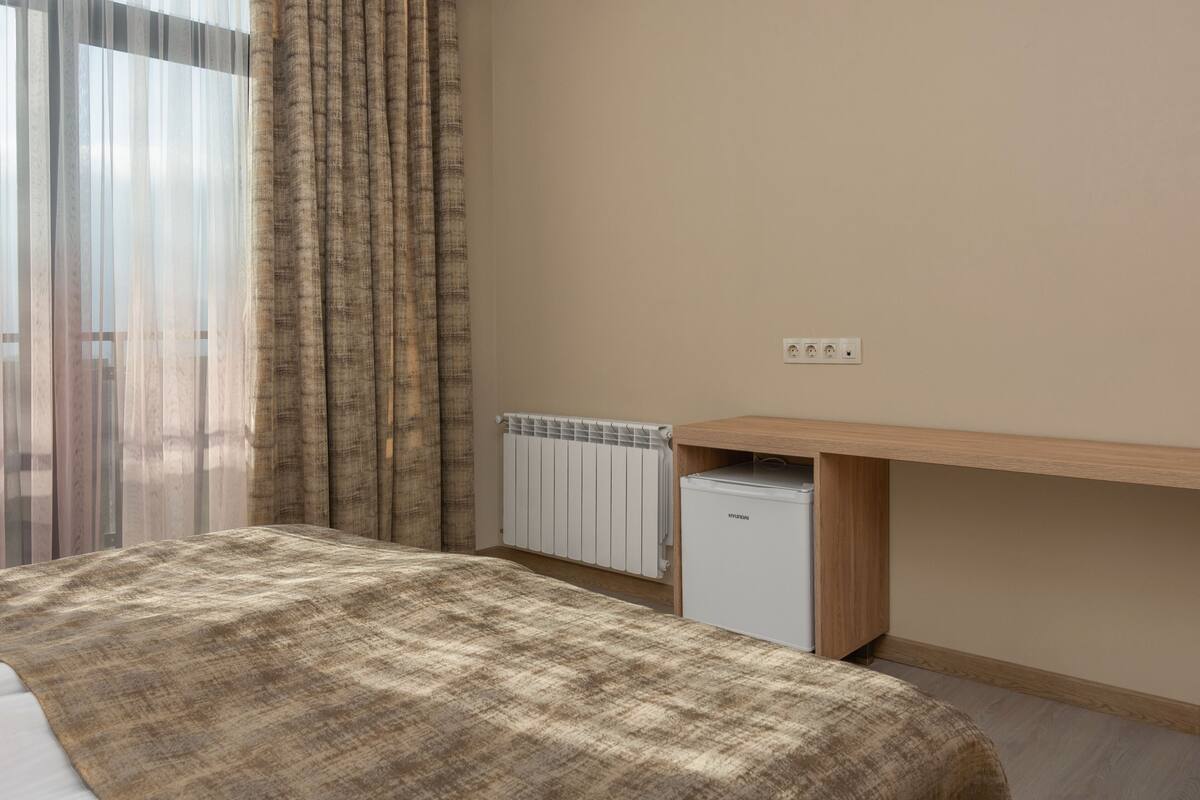Un dormitorio con cama, un radiador, un escritorio y una ventana con cortinas.