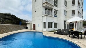 A swimming pool with lounge chairs and a table, surrounded by a building with balconies. - Oceanfront apartment, swimming pool, automatic check-in (Guayaquil)