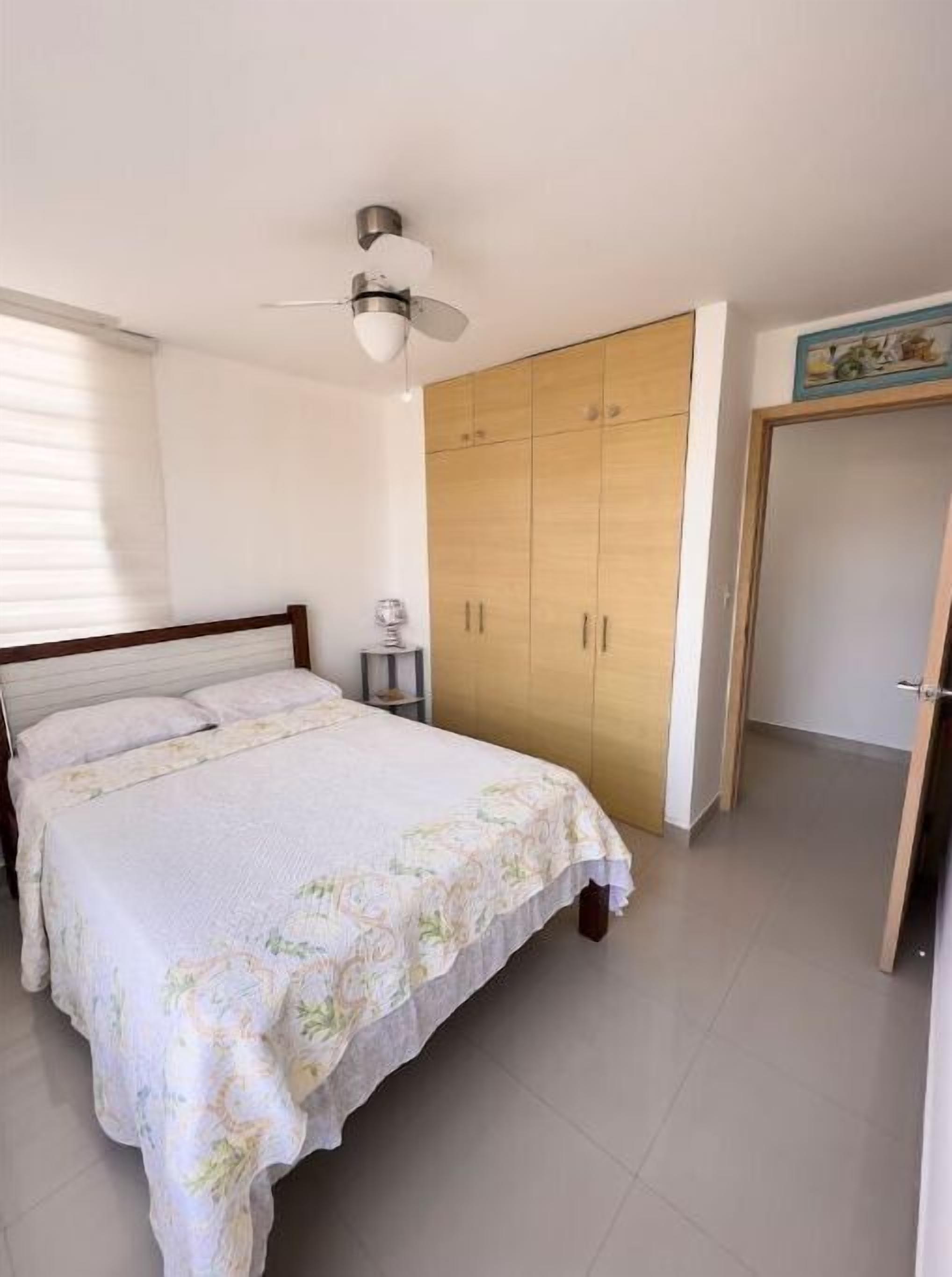 A bedroom with a bed, a wardrobe, a ceiling fan, and a window with blinds.