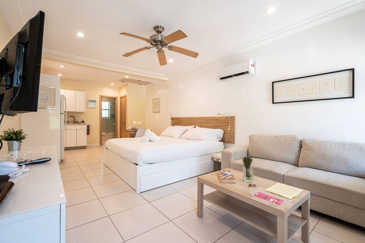A modern hotel room with a bed, a sofa, a desk with a telephone, a coffee table, and a ceiling fan.