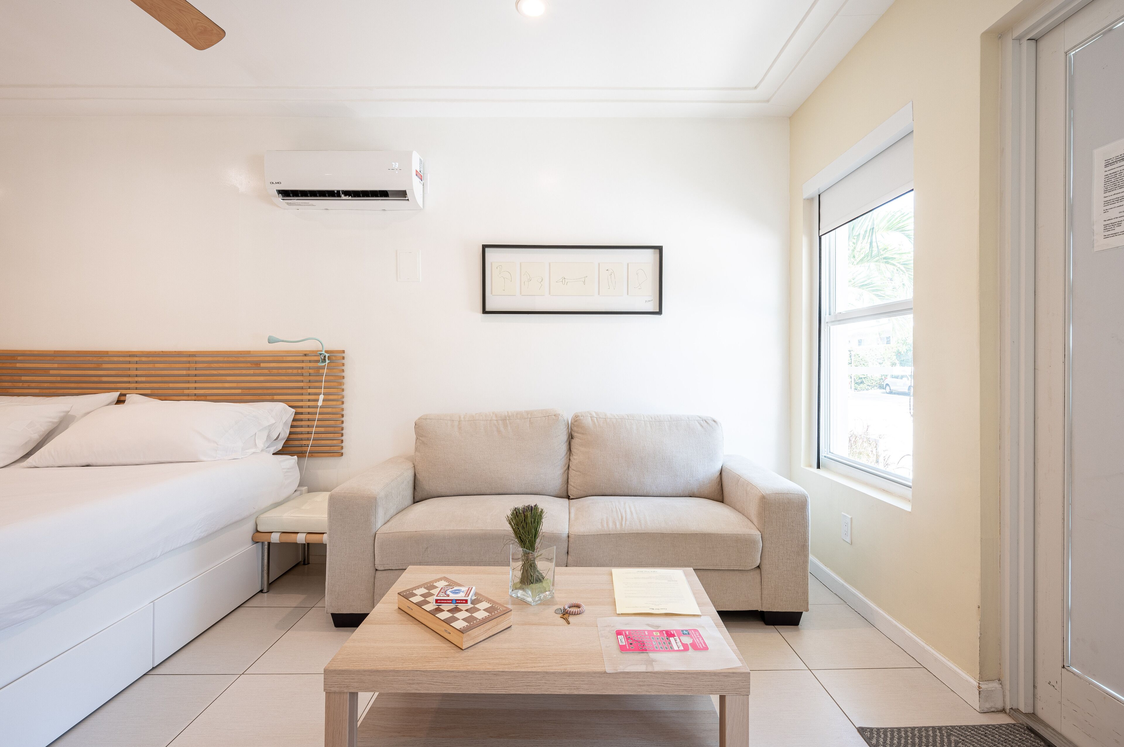 Una habitación de hotel moderna con cama, sofá, una mesa de centro con un tablero de ajedrez y un cuadro en la pared.