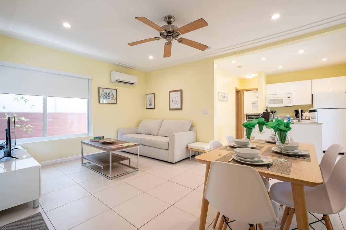 A modern living room with a sofa, coffee table, dining table set for two, and a ceiling fan.