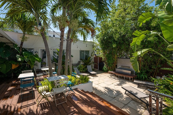 A patio area with outdoor seating, palm trees, and lush greenery.