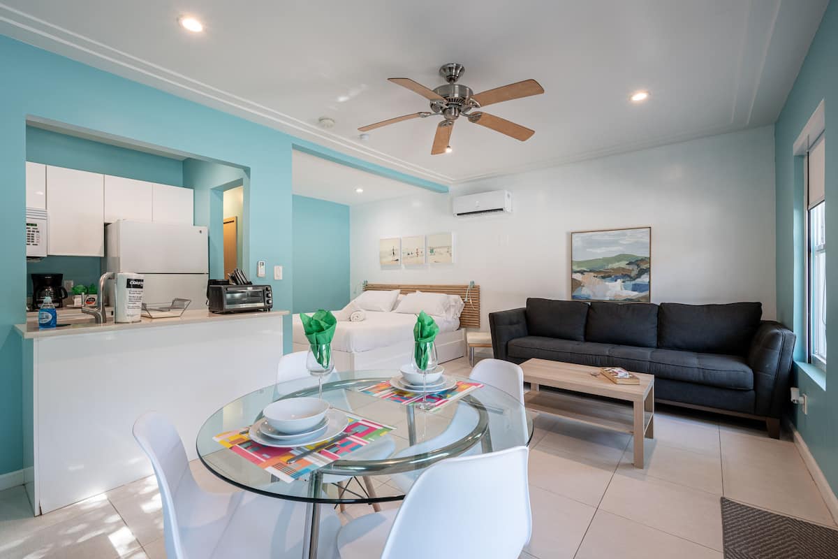 A modern living room with a glass dining table, a sofa, and a ceiling fan.