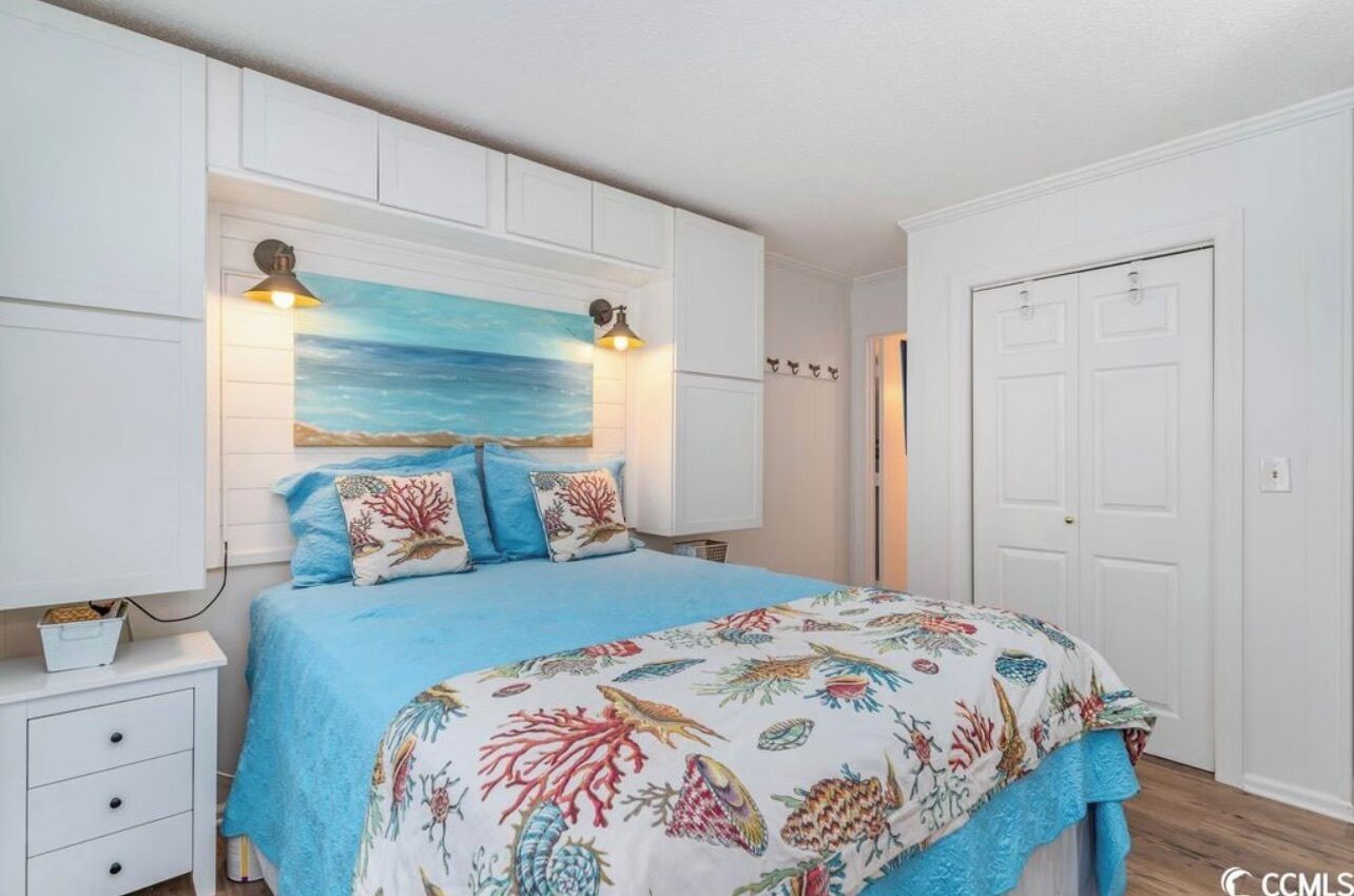 A bedroom with a bed, a nightstand, a wall-mounted lamp, and a door.