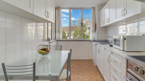 A modern kitchen with white cabinets, a glass dining table, and a view of the outside. - Refugio Madeirense by Atlantic Holiday (Funchal)