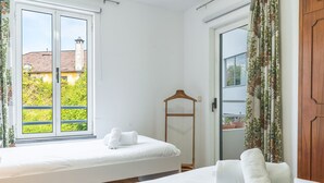 A bedroom with a bed, a wooden hanger, and a view of greenery outside. - Refugio Madeirense by Atlantic Holiday (Funchal)