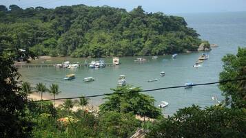 Zona costera con barcos amarrados cerca de una isla boscosa, una playa de arena y abundante vegetación.