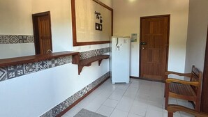 A spacious kitchen with a tiled backsplash, a refrigerator, wooden cabinets, and a dining area with a chair. - Flats e suítes nativa (Paraty)