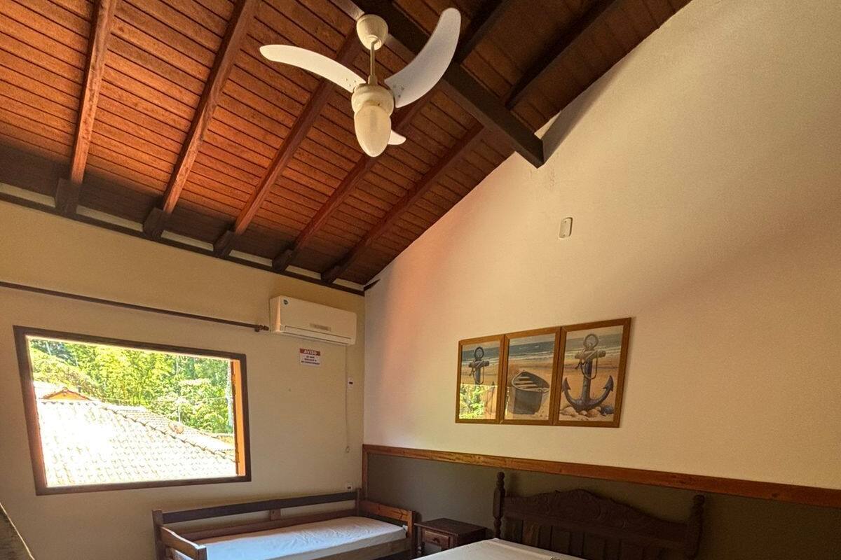 Une chambre à coucher comprenant un lit, un banc, un ventilateur de plafond, une fenêtre et un réfrigérateur.