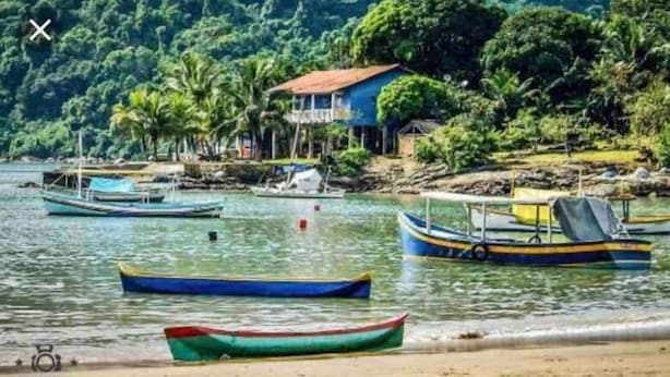 A coastal scene with boats docked near a house surrounded by lush greenery. - Flats e suítes nativa (Paraty)
