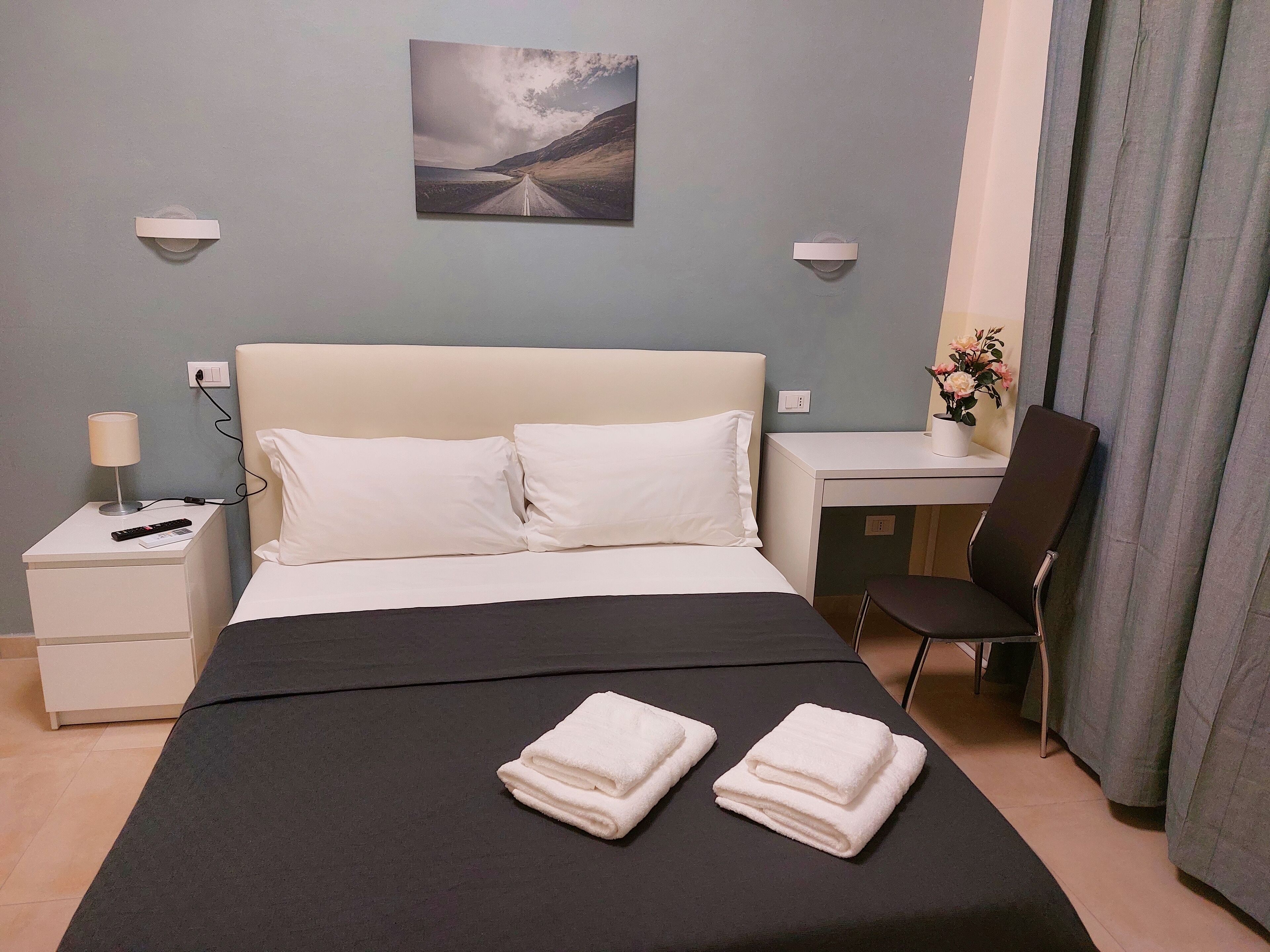 Hotellihuone, jossa on sänky, työpöytä, tuoli, lamppu ja taulu seinällä.
