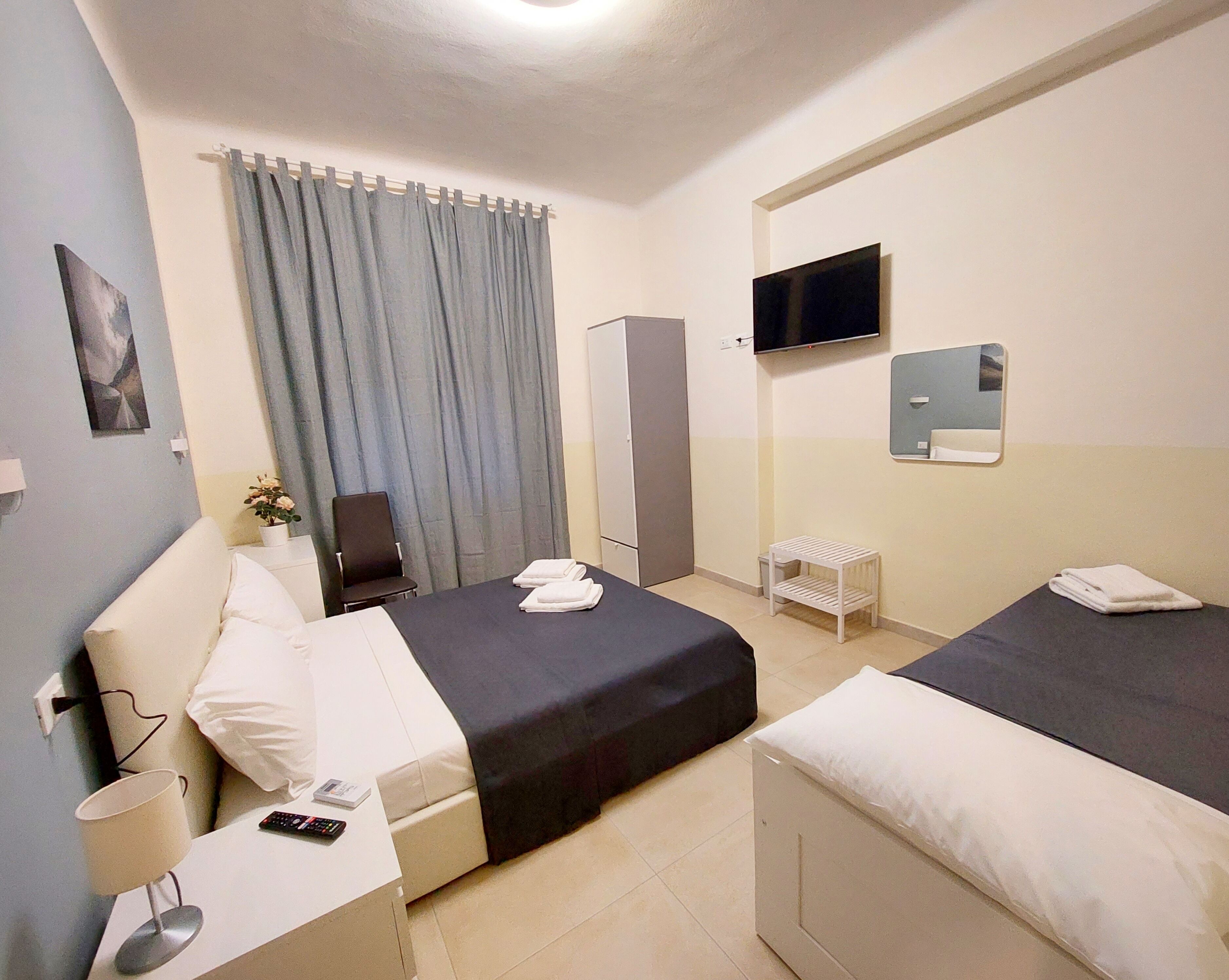 A hotel room with two beds, a TV, a mirror, a desk with a lamp, and a chair.