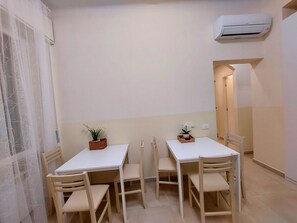 A small dining area with two white tables and four wooden chairs, each table with a small potted plant. - Bonaini Relax B&B (Pisa)