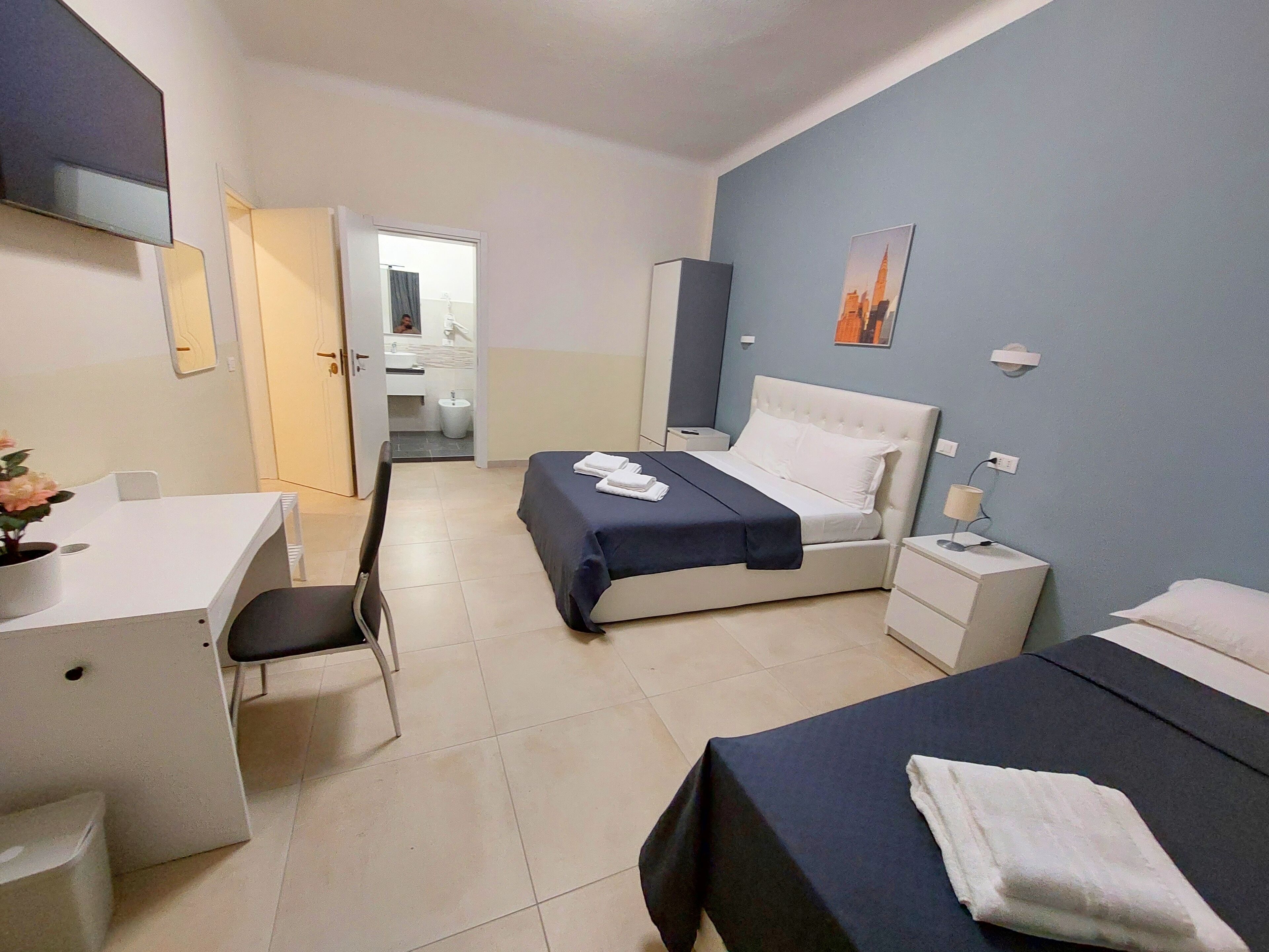 A hotel room with a bed, a desk, a chair, a nightstand, and a bathroom visible through an open door.