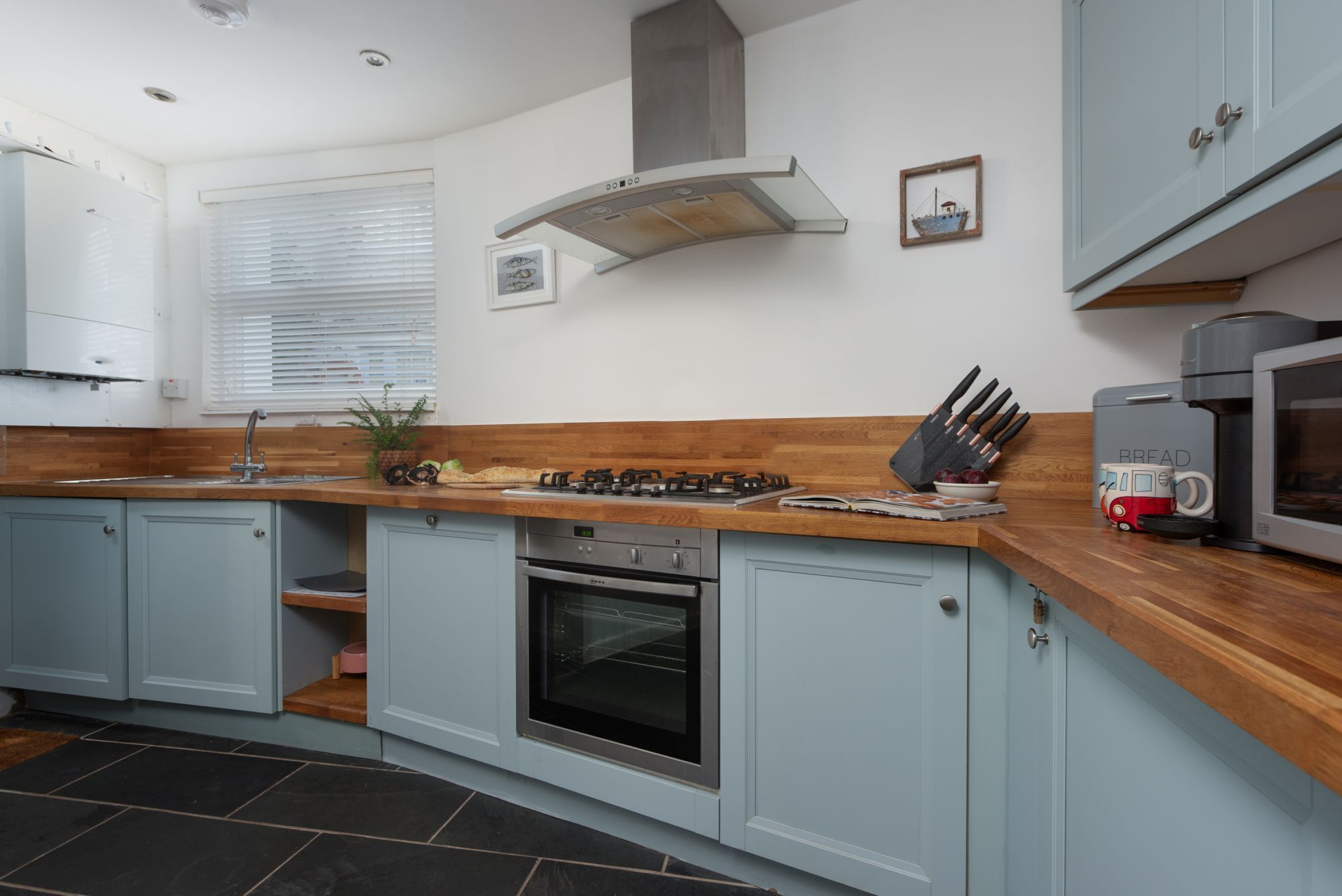 A kitchen with light blue cabinets, a wooden countertop, a gas stove, an oven, and a microwave.