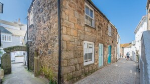 Une ruelle étroite pavée de pierres, bordée de bâtiments en pierre, avec une porte bien visible et une petite arche.