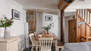 Un coin repas rustique avec une table en bois, des chaises blanches et un mur en pierre. Une pancarte sur la porte indique : « Plage de Portmeadow ».
