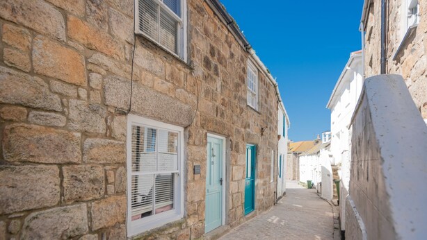 Une ruelle étroite pavée, bordée de bâtiments en pierre aux portes blanches et bleues.