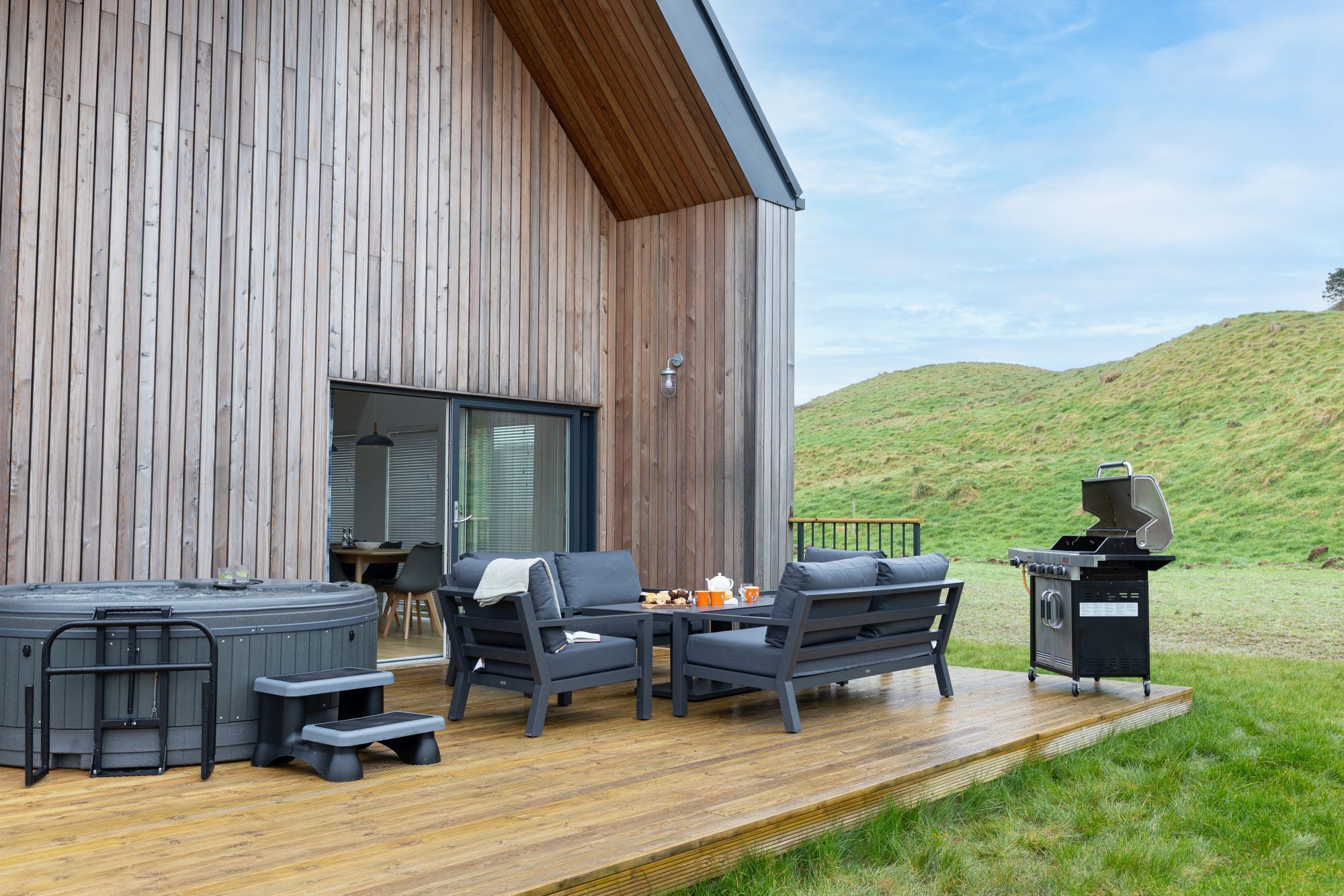 An outdoor deck with a hot tub, seating area, and a barbecue grill.