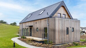 Une maison moderne en bois, dotée d’un toit en pente, de grandes fenêtres et d’un balcon.