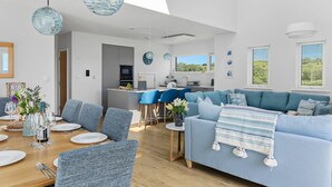 Una cocina moderna con armarios grises, un comedor con una mesa de madera dispuesta para cuatro personas y un sofá azul en la sala de estar.