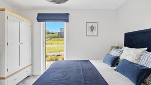 Un dormitorio con cama, armario, ventana que ofrece vistas a zonas verdes y edificios, y ventilador de techo.