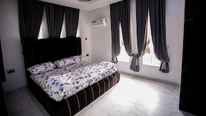 Une chambre à coucher avec un lit, des rideaux occultants, un climatiseur et un sol carrelé.