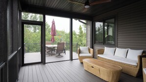Une terrasse extérieure couverte, aménagée avec des meubles en osier, une table et un ventilateur de plafond.