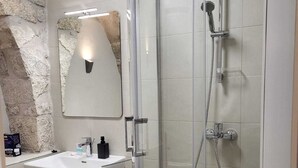 Une salle de bain moderne avec une douche à parois de verre, un lavabo blanc avec un miroir au-dessus et un mur d’accent en pierre.