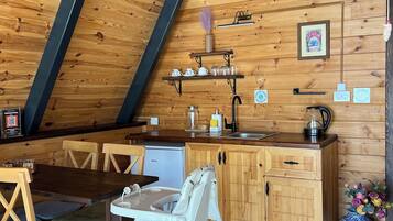 Una cocina acogedora con paredes de madera, una zona de comedor con sillas, un refrigerador pequeño y una silla blanca.