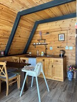 Una cocina acogedora con paredes de madera, una zona de comedor con sillas, un refrigerador pequeño y una silla blanca.
