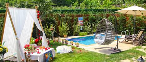 Un patio trasero con piscina, una silla colgante y una mesa con un cuadro.