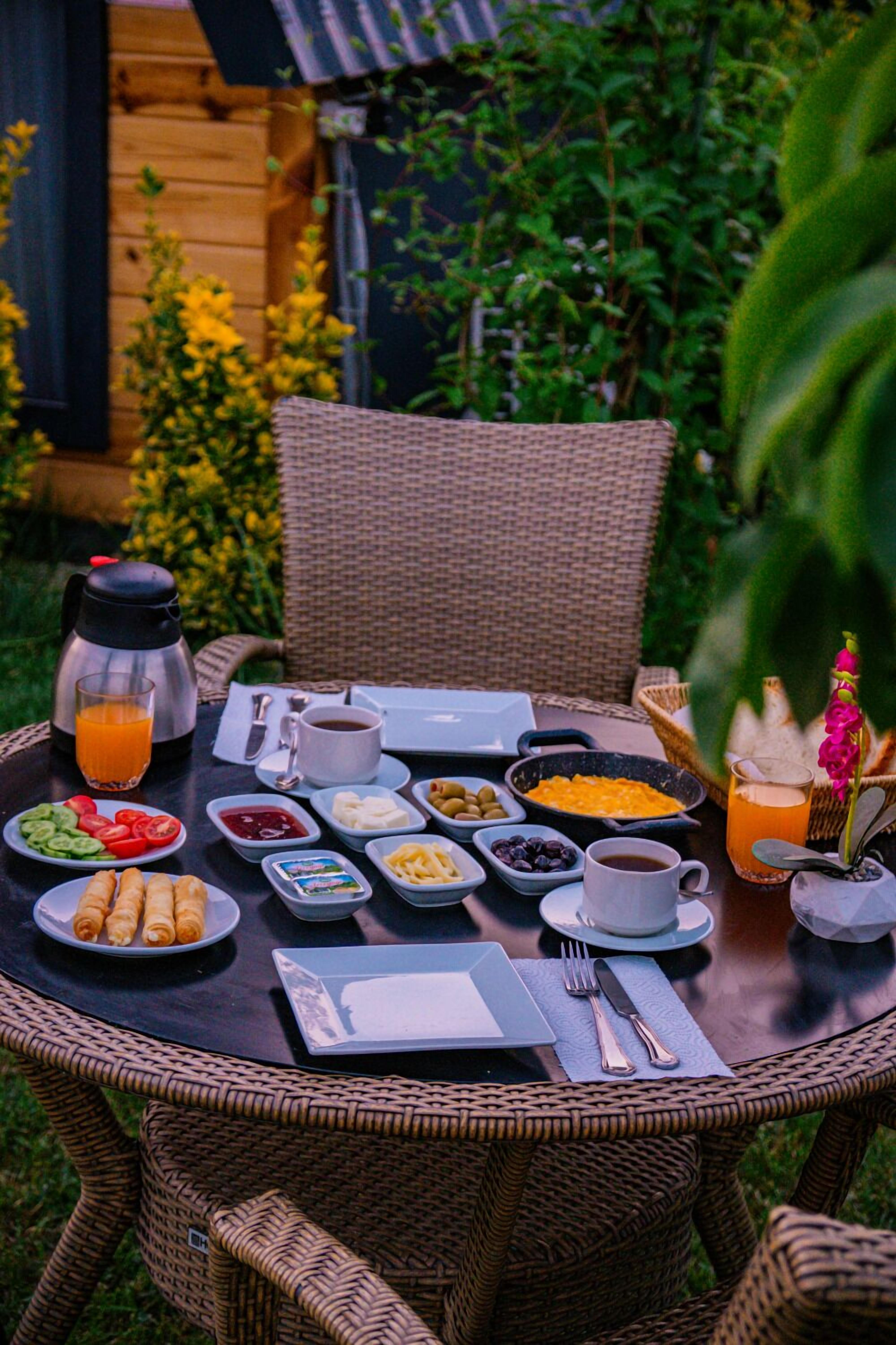 Una mesa redonda de mimbre dispuesta para el desayuno, con platos de comida, una cafetera y un vaso de jugo de naranja.
