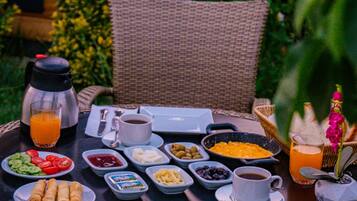 Una mesa redonda de mimbre dispuesta para el desayuno, con platos de comida, una cafetera y un vaso de jugo de naranja.