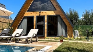 Un edificio moderno triangular con piscina, sillones de descanso y un cielo azul despejado.