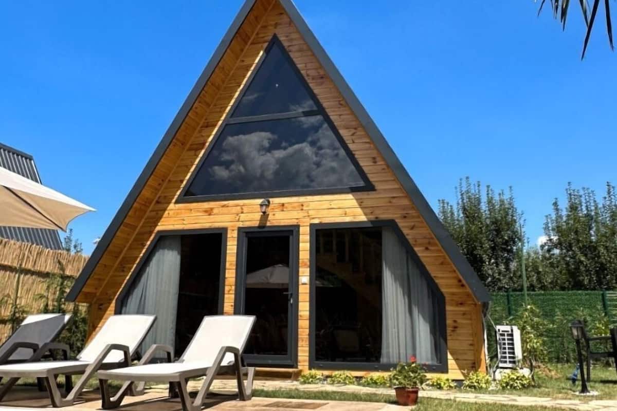 A modern triangular building with a pool, lounge chairs, and a clear blue sky.