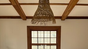 Ett rum med en beige soffa, ett träpanelat tak, ett fönster med ett rutmönster och en hängande lampa.