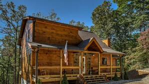 A wooden cabin with a porch, a flag, and a small Christmas tree. - Raven’s Retreat: Sauna, Putting Green & Arcade! (Blue Ridge)